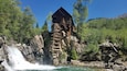 A wooden watermill with a waterfall in a forested area.