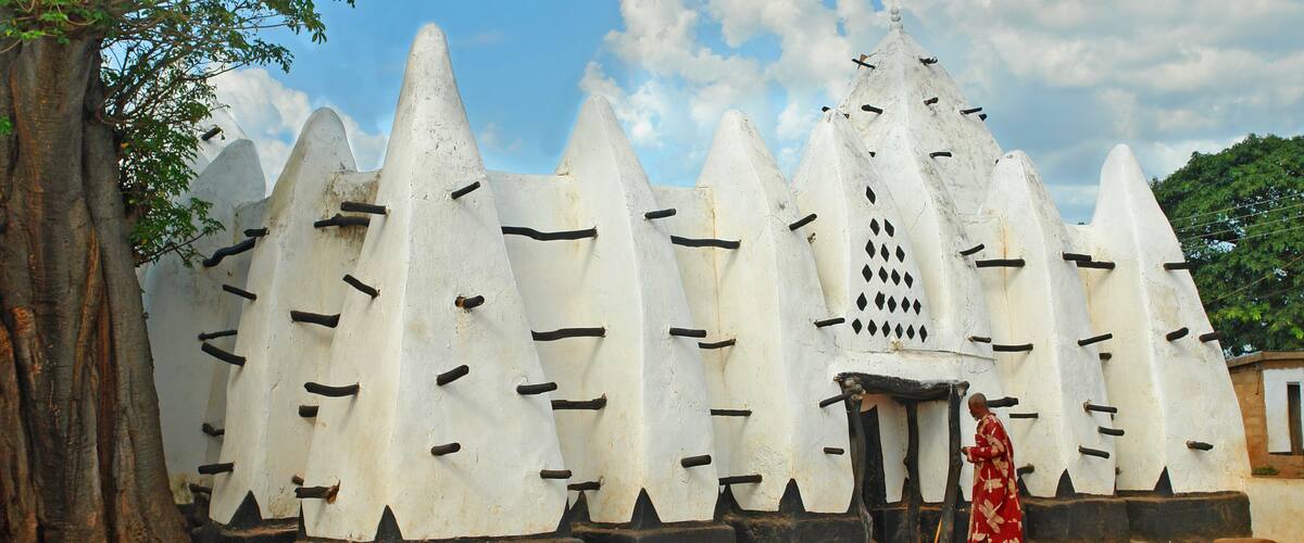 A traditional building with a unique conical roof design, surrounded by a large tree and a clear sky.