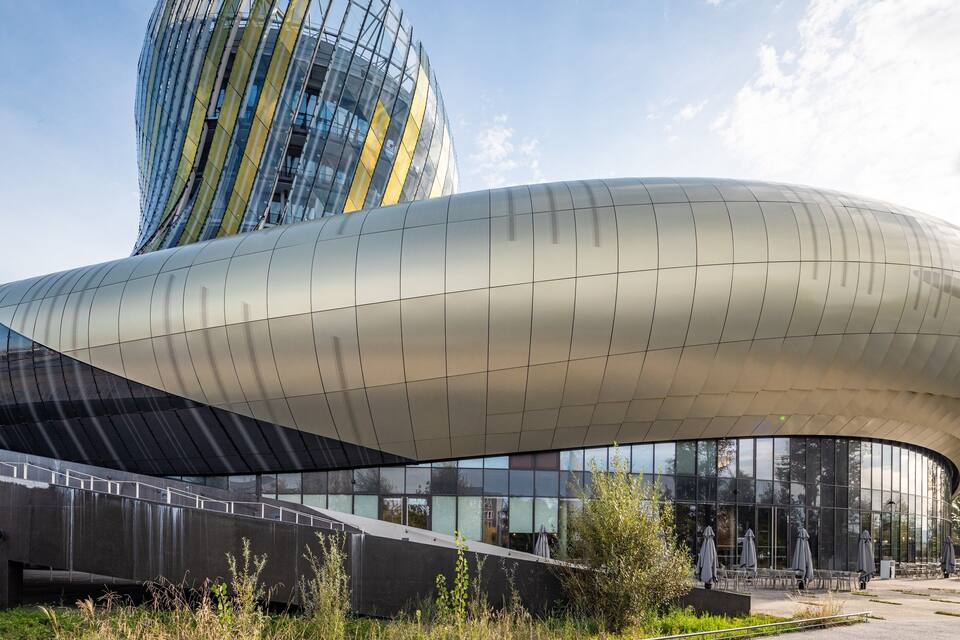 Une structure architecturale moderne, dotée d’une façade métallique incurvée et d’un bâtiment en verre réfléchissant en arrière-plan.