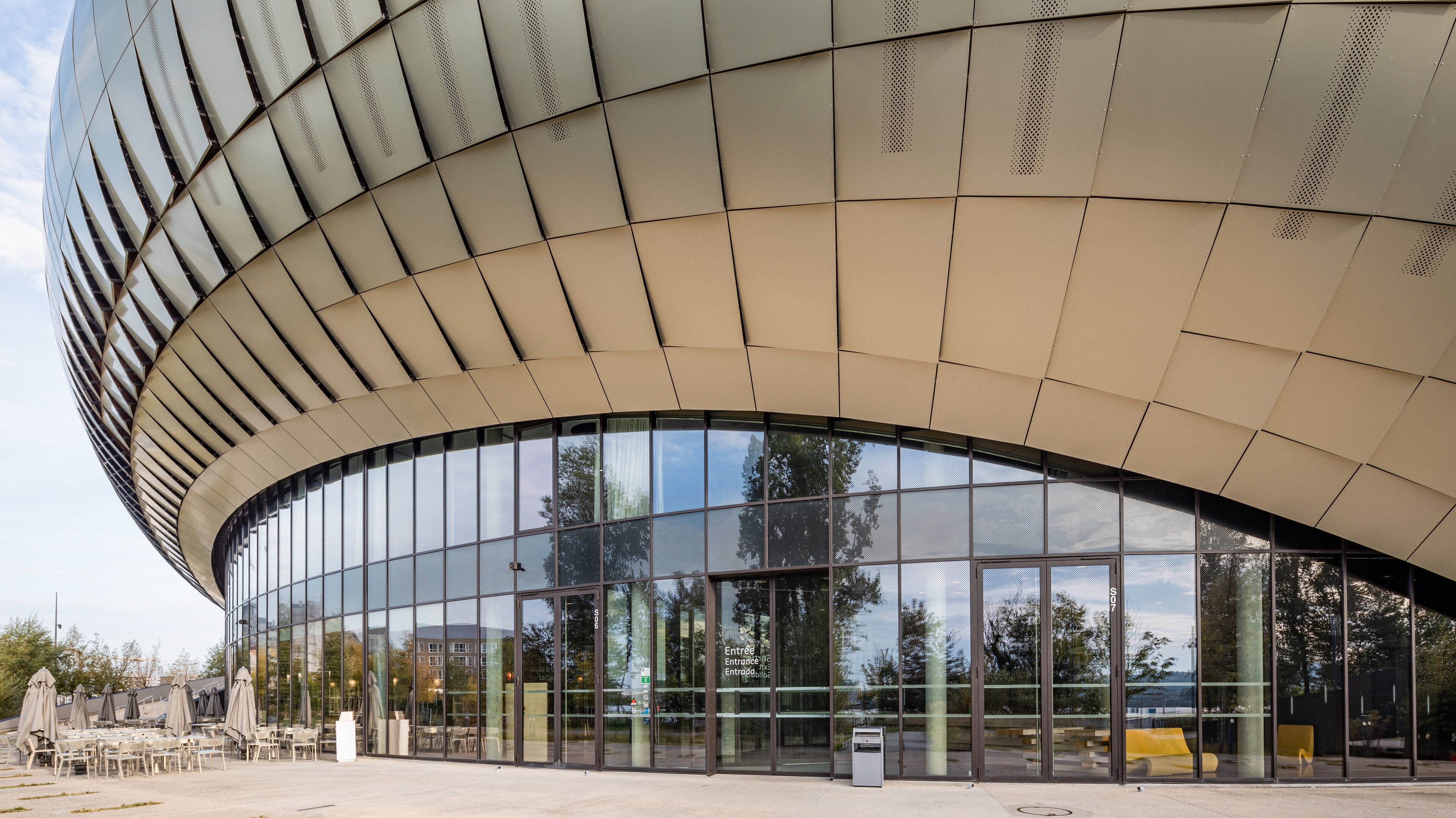 A modern building with a curved glass facade and a metal roof.