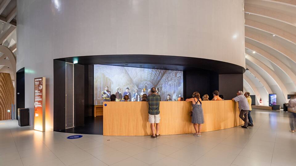 A modern building interior with a curved reception desk, a large digital display, and a high ceiling with a ribbed design.