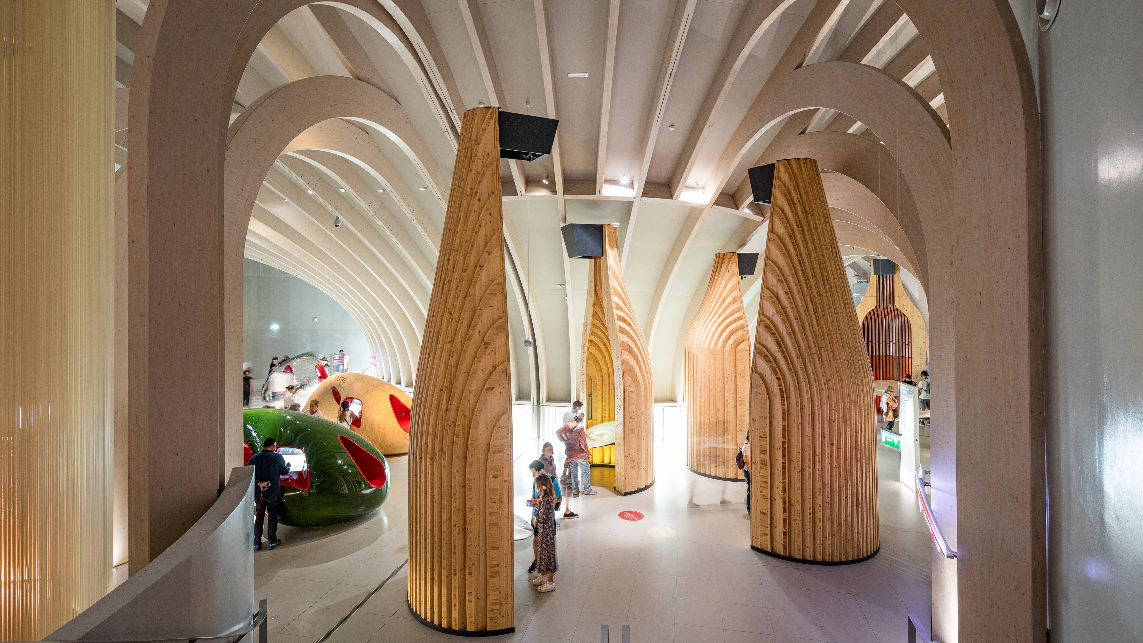 A modern architectural interior with curved wooden columns and a green, futuristic structure.