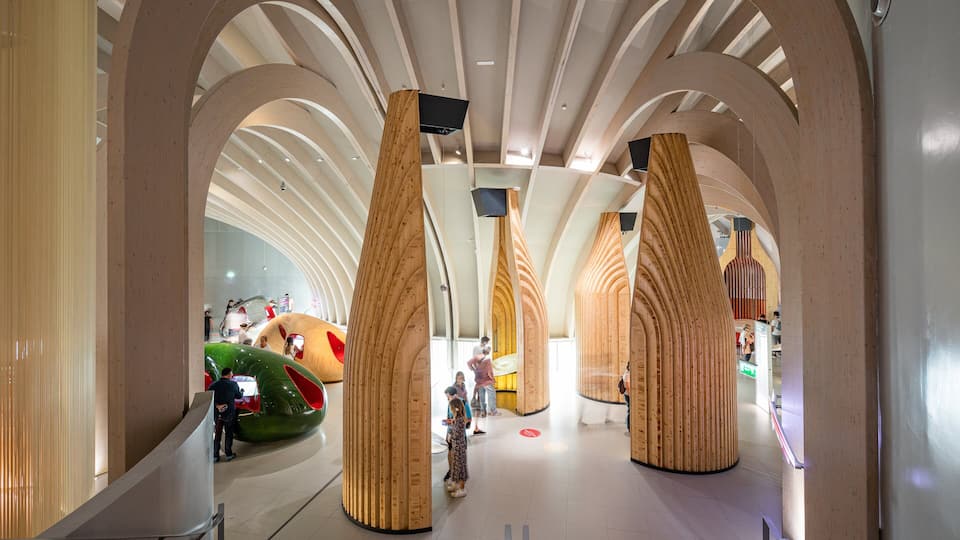 A modern architectural interior with curved wooden columns and a green, futuristic structure.
