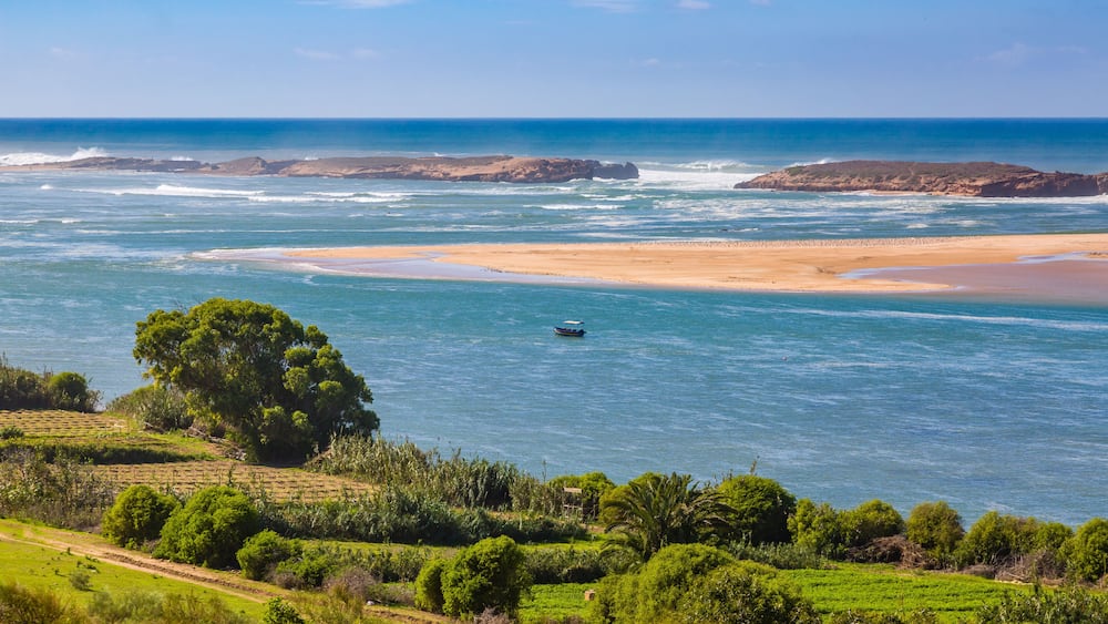 Un paysage côtier avec une plage de sable, des affleurements rocheux et un petit bateau sur l’eau.