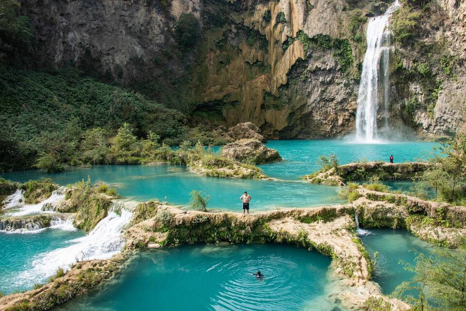 A waterfall cascading into a turquoise pool surrounded by rocky terrain and greenery.