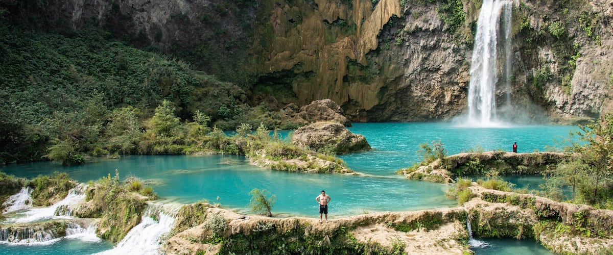 A waterfall cascading into a turquoise pool surrounded by rocky terrain and greenery.
