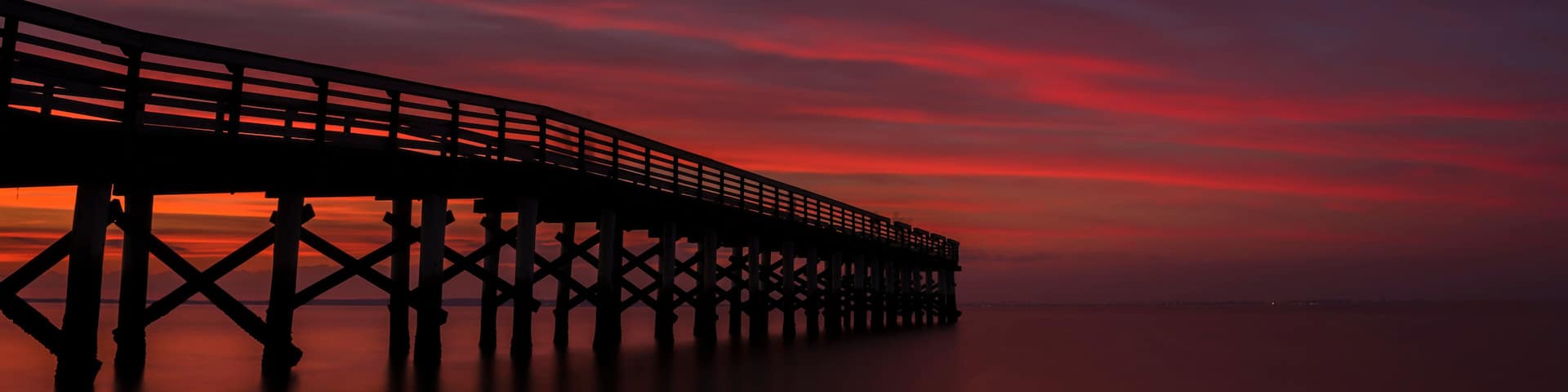 Dramatic red sunset viewed from Bayshore Waterfront Park, New Jersey featuring fishing pier on the background
