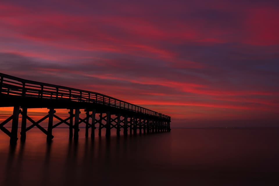 Un muelle se adentra en aguas tranquilas al atardecer, con un cielo lleno de color.