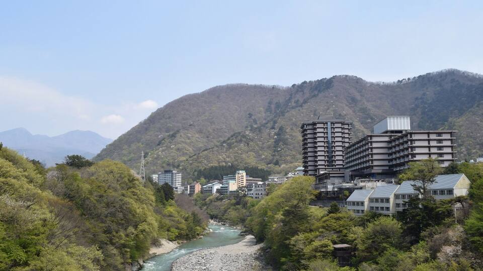 A river flowing through a valley with buildings and mountains in the background.