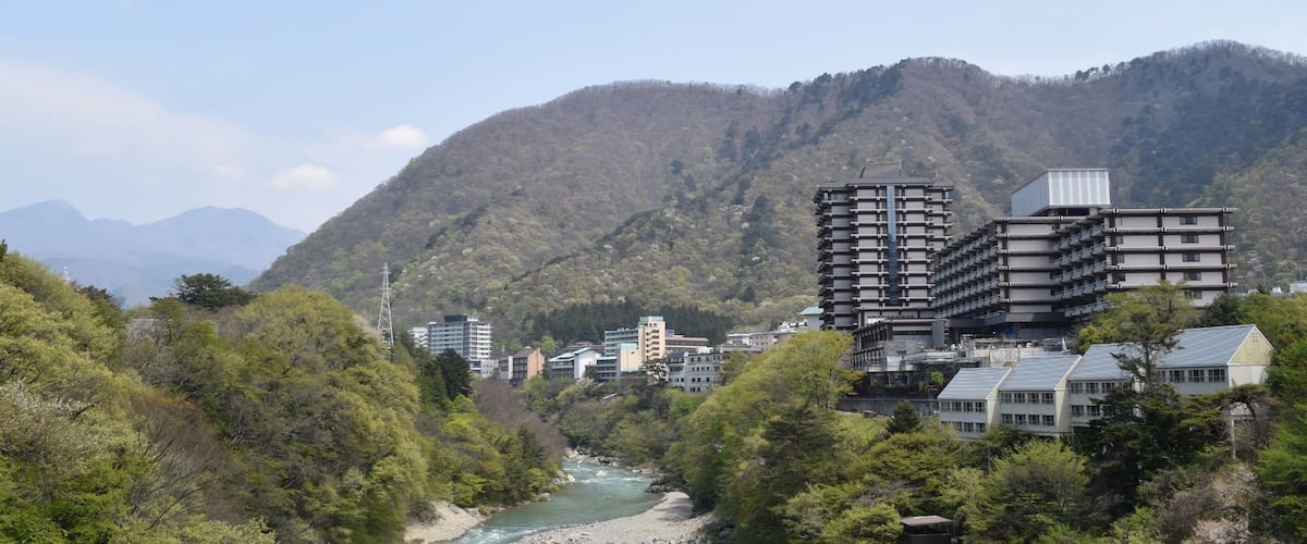 A river flowing through a valley with buildings and mountains in the background.