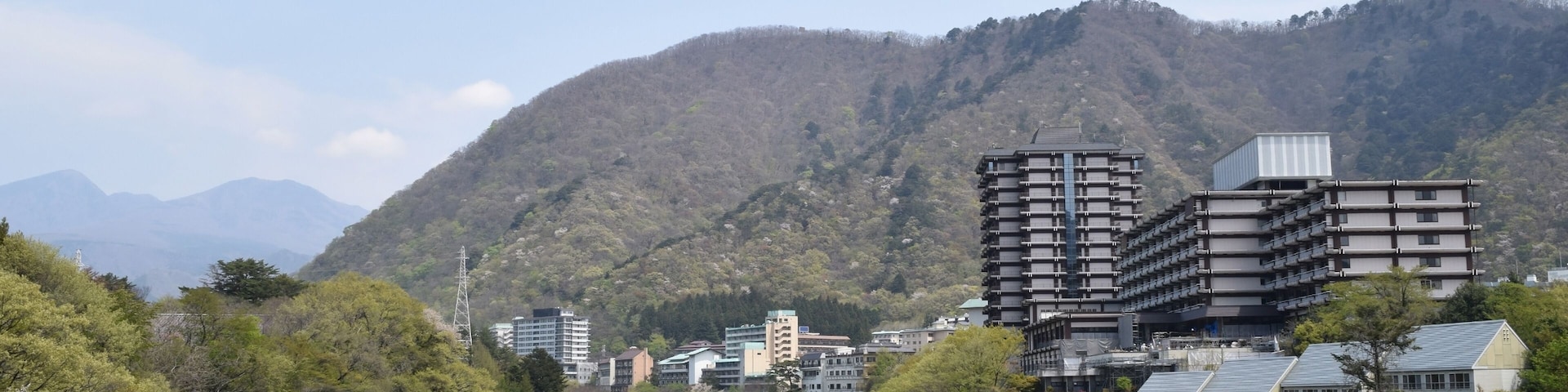 A river flowing through a valley with buildings and mountains in the background.