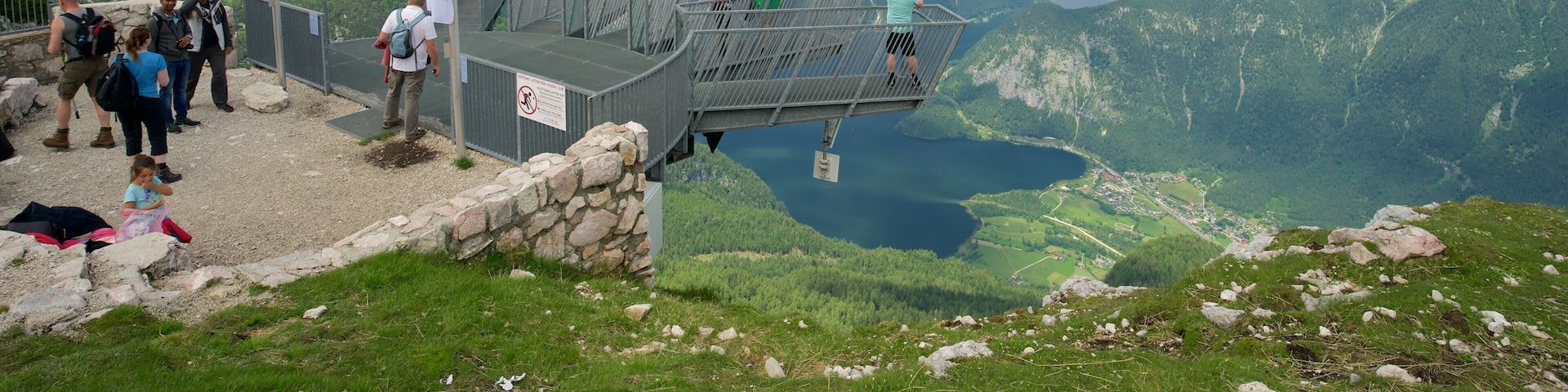 A scenic overlook with a metal platform, flags, and a mountainous landscape with a lake below.