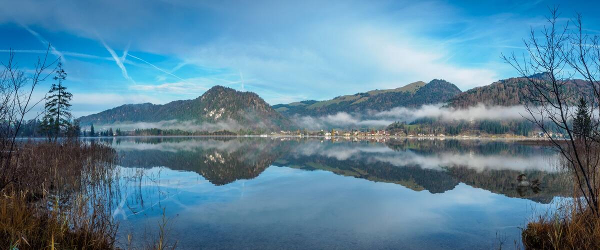 A calm lake reflecting mountains and a misty forest.