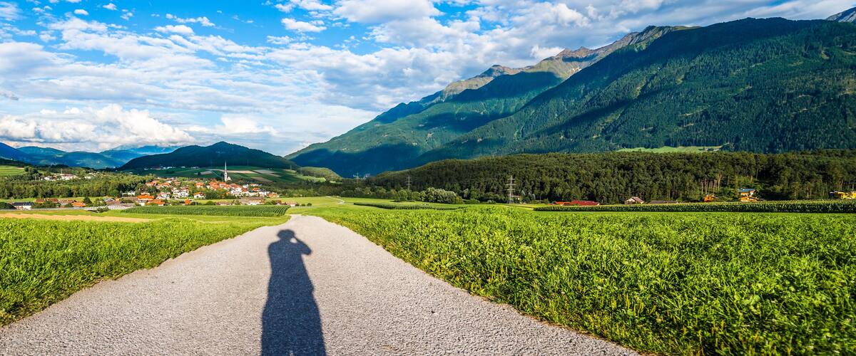 A road leading through a valley with mountains on either side and a small village in the distance.