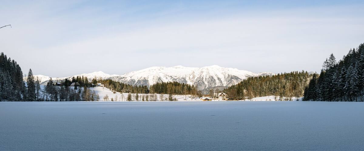 A snow-covered lake with mountains in the background and dense forests on either side.