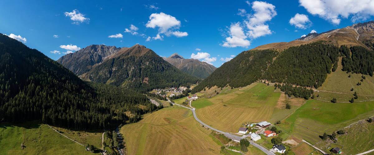 A mountainous landscape with a village nestled in a valley, surrounded by forests and fields.