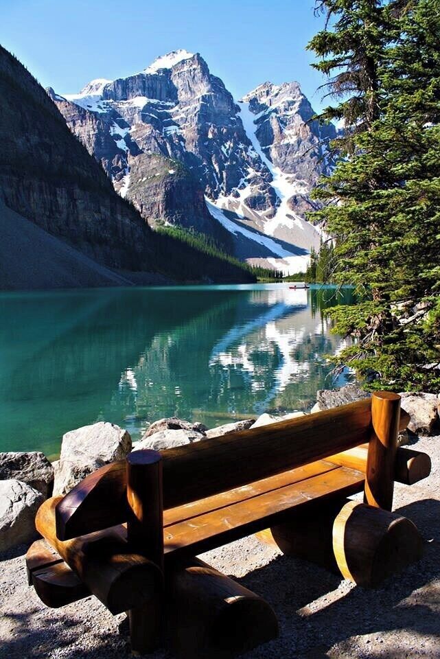 A wooden bench by a clear turquoise lake with mountains in the background.