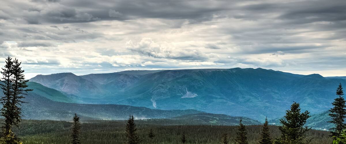 A mountainous landscape with dense forests and a cloudy sky.