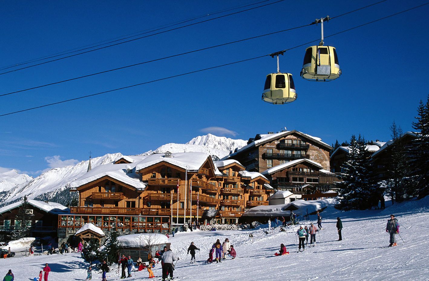 A ski resort with wooden buildings, a ski lift, and snow-covered mountains in the background.