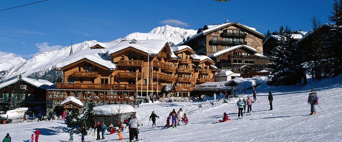 A ski resort with wooden buildings, a ski lift, and snow-covered mountains in the background.