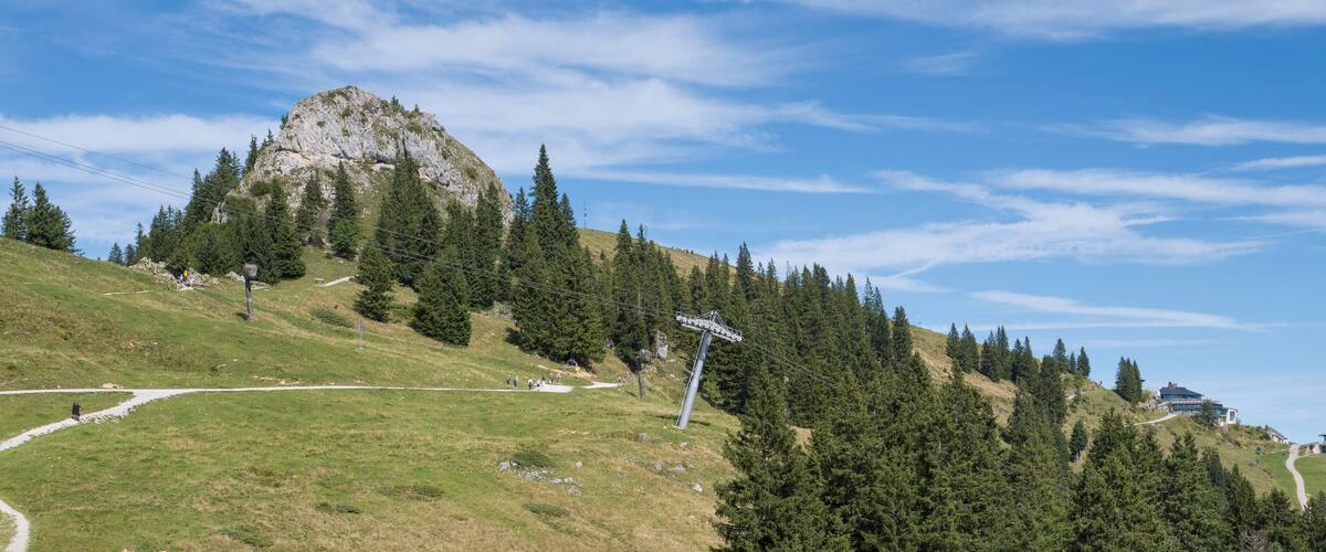 A mountain landscape with a ski lift, a rocky peak, and a building on the right.