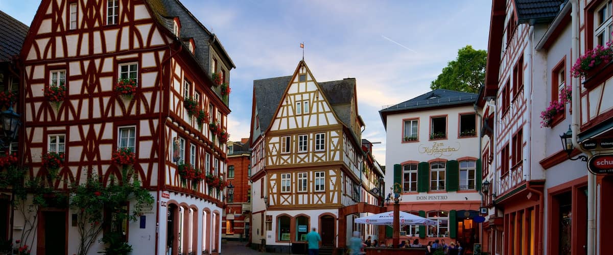 A cobblestone street lined with traditional half-timbered buildings, a sign for Zum Kirchgarten, and a BINDING restaurant.