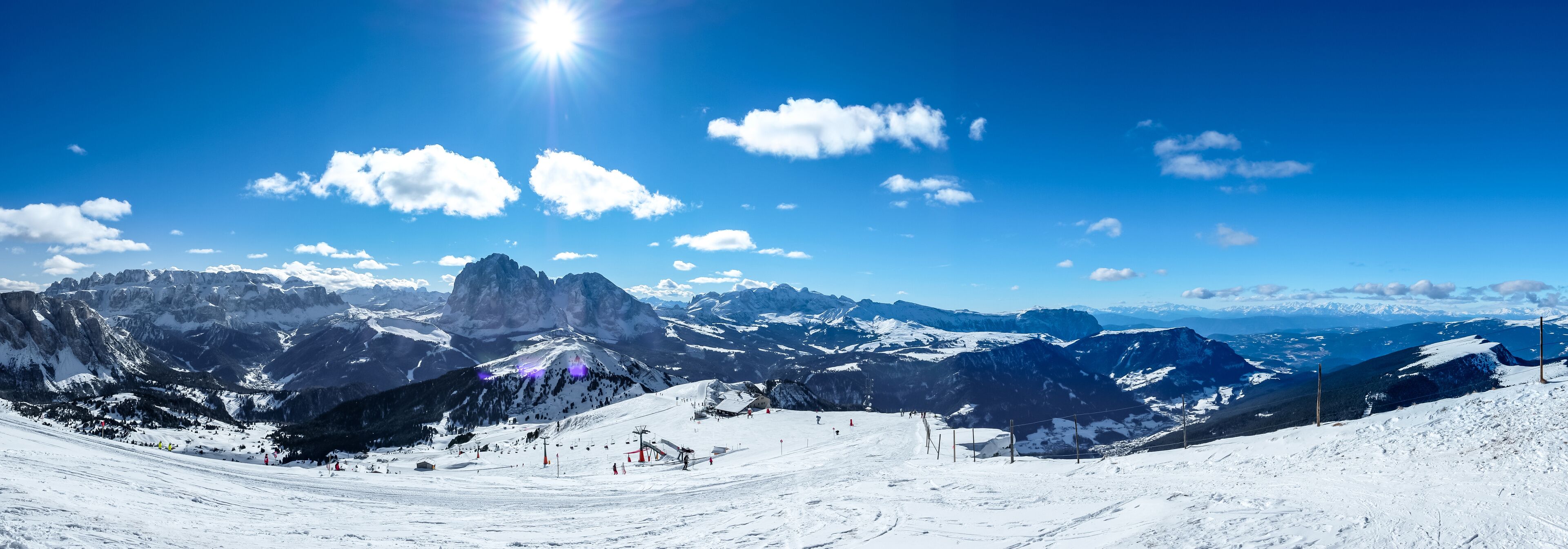 A snow-covered mountain landscape with ski slopes, a prominent peak, and a clear blue sky.