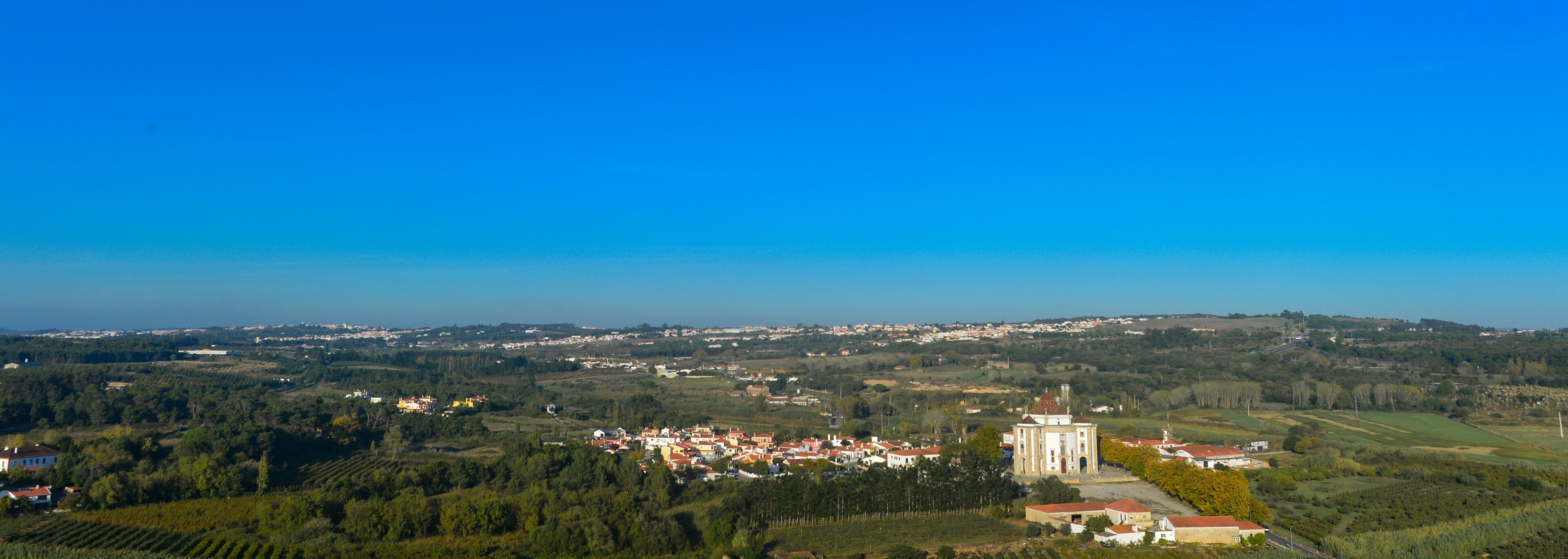 Uma cidade costeira com uma igreja imponente, vinhedos e colinas suaves ao fundo.