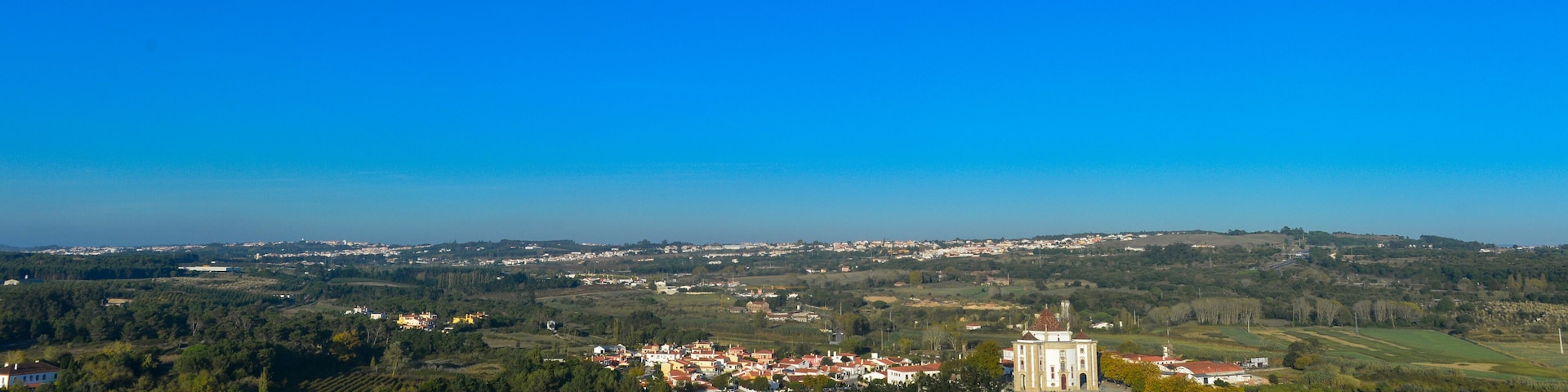 Uma cidade costeira com uma igreja imponente, vinhedos e colinas suaves ao fundo.