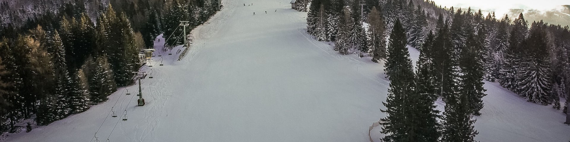 Aerial view of a ski slope, with heavy clouds in the background. Cerkno ski slope in Slovenia, with a ski lift visible on the left.