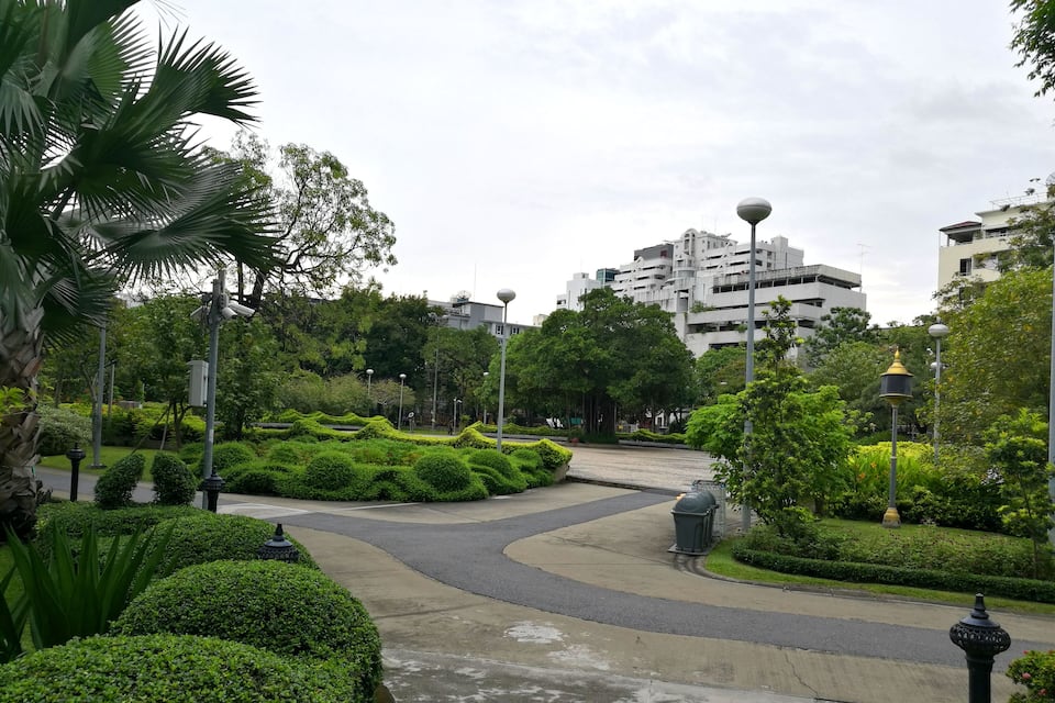 A landscaped park with manicured bushes, a curved pathway, and modern street lamps.
