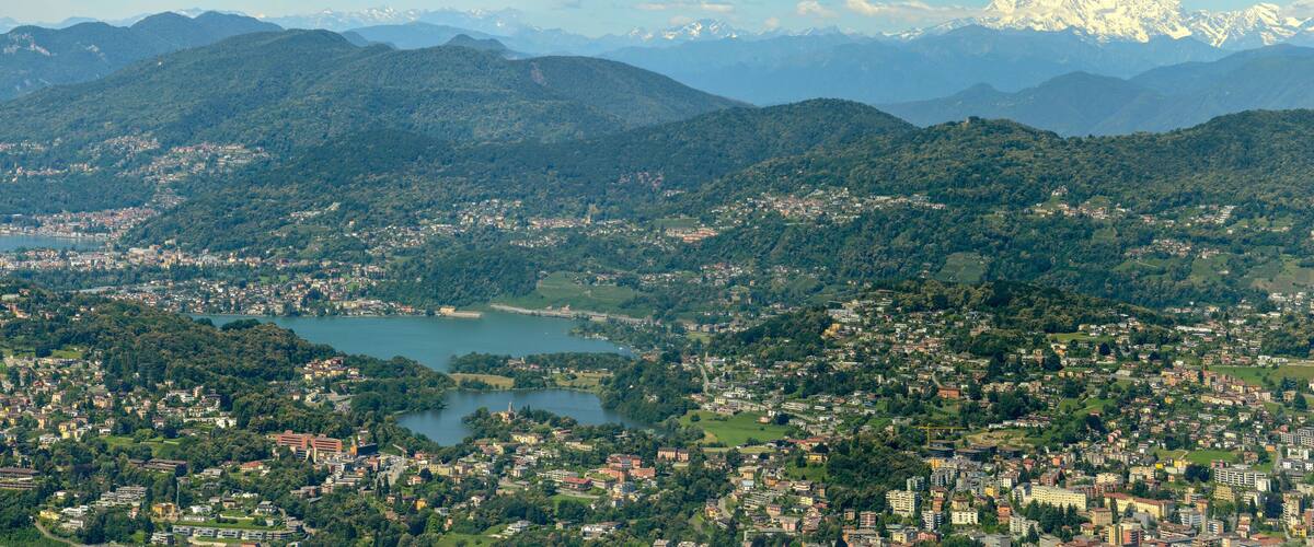 A mountainous landscape with a town nestled among hills, a lake, and distant snow-capped peaks.