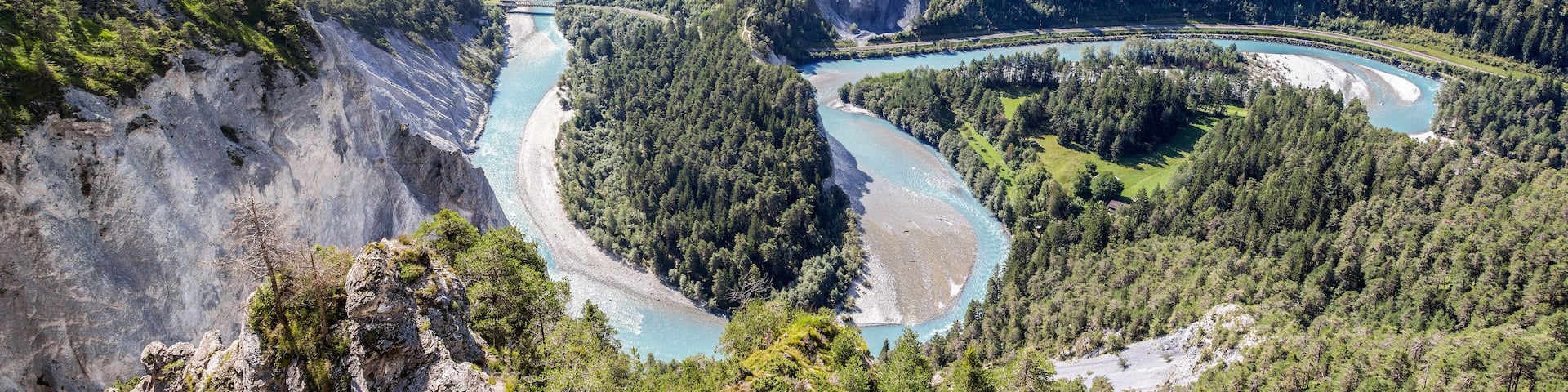 A river winding through a mountainous forest with a bridge and a road.