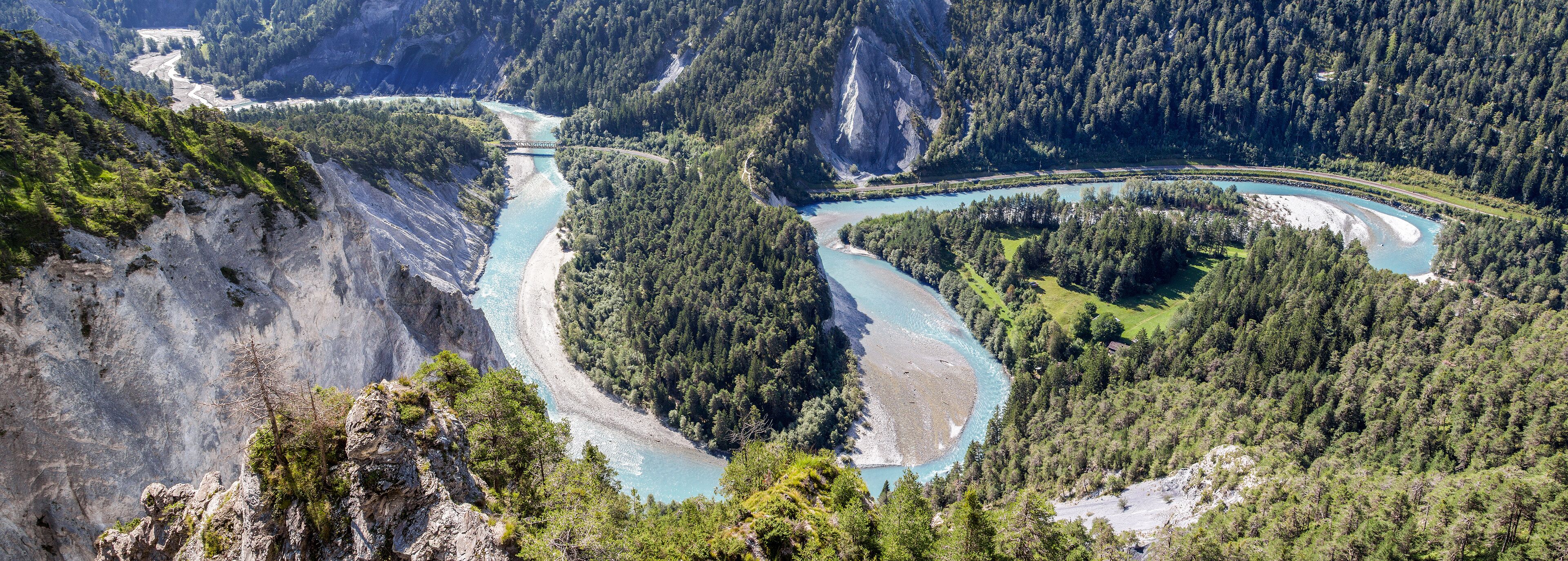 A river winding through a mountainous forest with a bridge and a road.