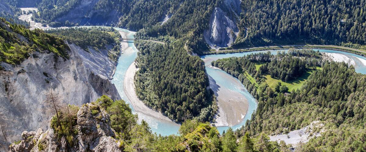 A river winding through a mountainous forest with a bridge and a road.