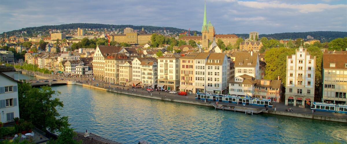 A riverside cityscape with historic buildings, a prominent church steeple, and a river with a boat.