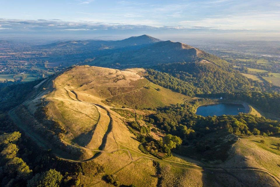 A mountainous landscape with a winding road, a lake, and a distant town.