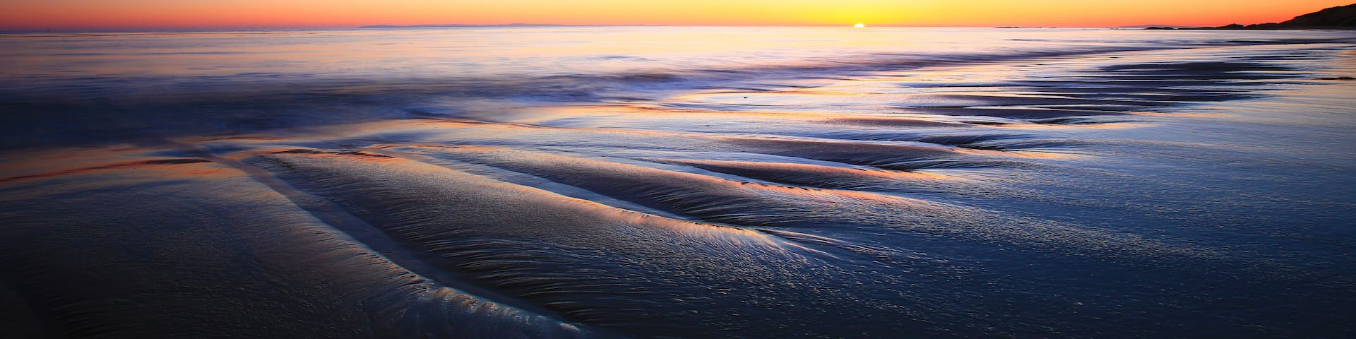 A beach at sunset with waves gently lapping onto the shore.