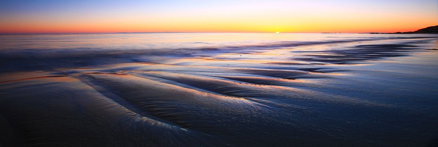 Uma praia ao pôr do sol, com ondas suaves beijando a costa.
