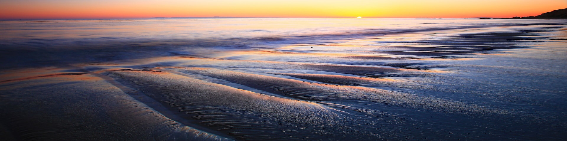 Ein Strand bei Sonnenuntergang, sanfte Wellen umspülen das Ufer.