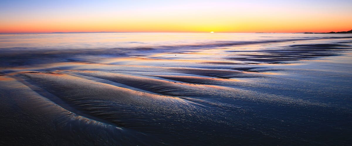A beach at sunset with waves gently lapping onto the shore.