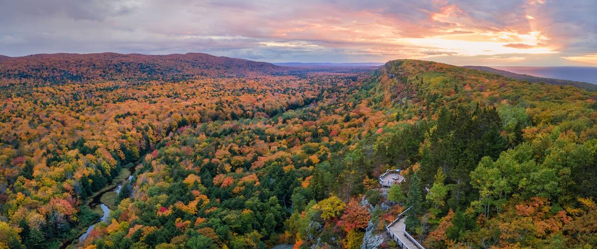A forested mountain range with a winding road and a small structure on a hill.