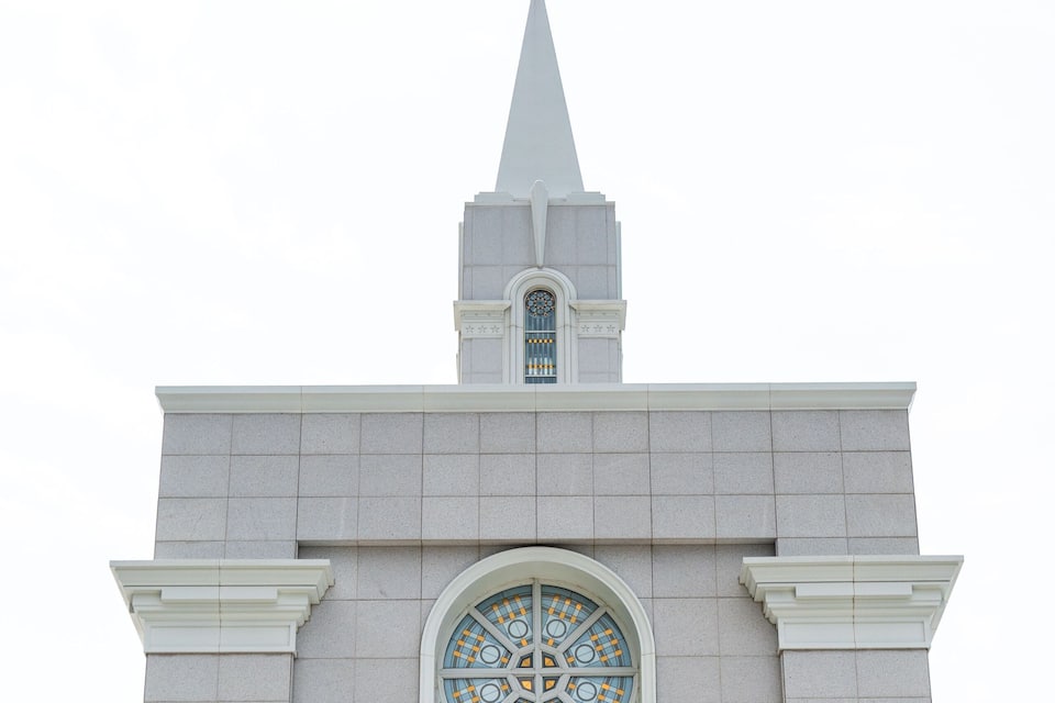 A building with a pointed roof, a large arched window with intricate patterns, and a golden statue on top.