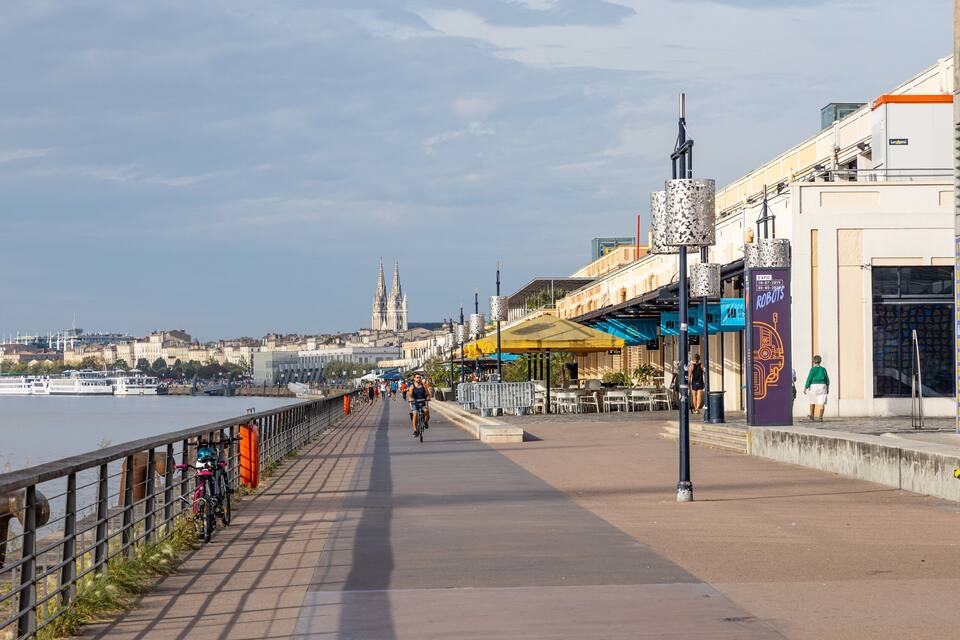 Un paseo ribereño con una catedral histórica al fondo, cafés al aire libre y un cartel para Expo 2013.