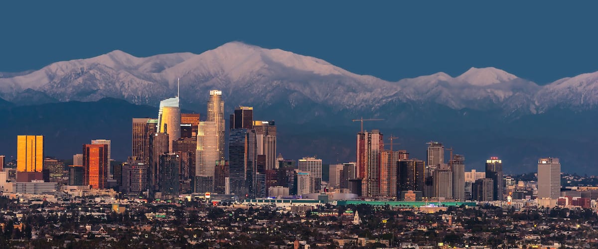 A city skyline with modern buildings and snow-capped mountains in the background.