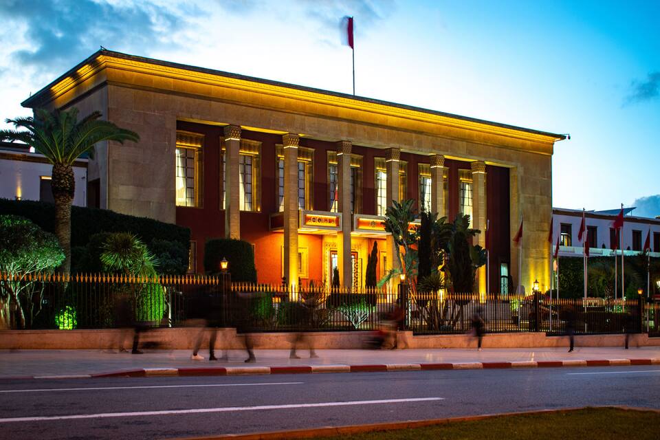 A large, well-lit building with columns, a flag, and a fence.
