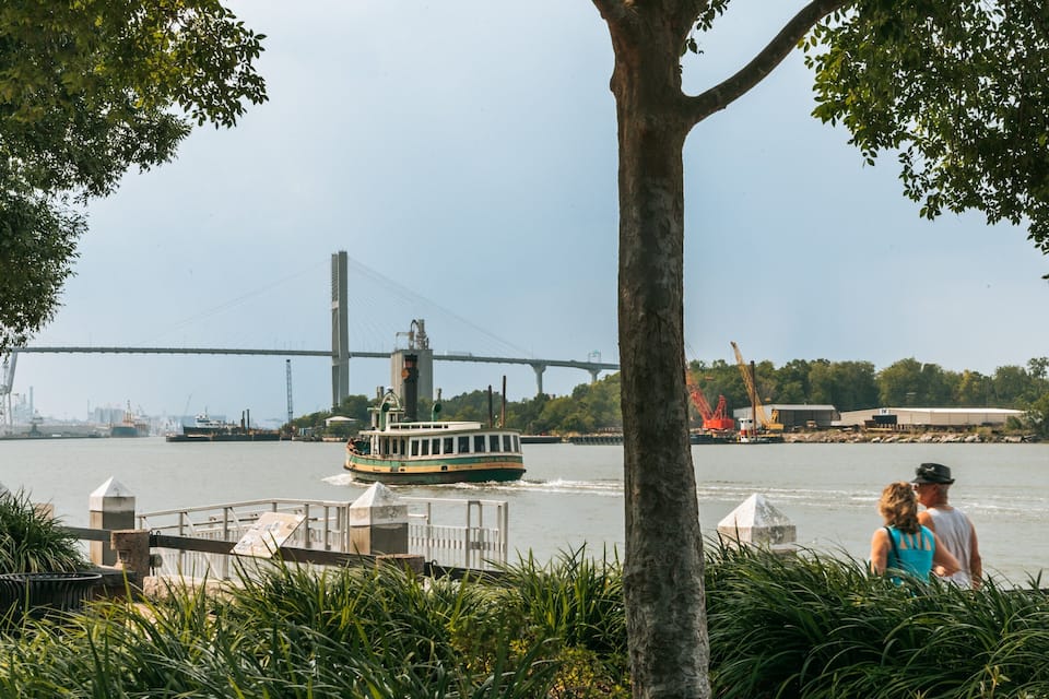 Ein Fluss mit einer Brücke, einem Boot und Spaziergängern am Ufer.