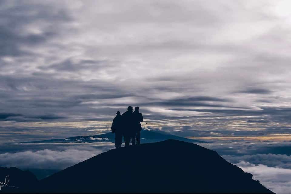 A mountain peak with a group of people standing at the summit, surrounded by clouds.