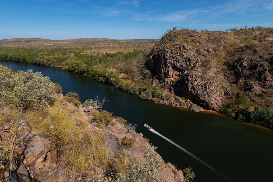 Een rivier kronkelt door een rotsachtig klooflandschap, met schaarse begroeiing en een heldere lucht.
