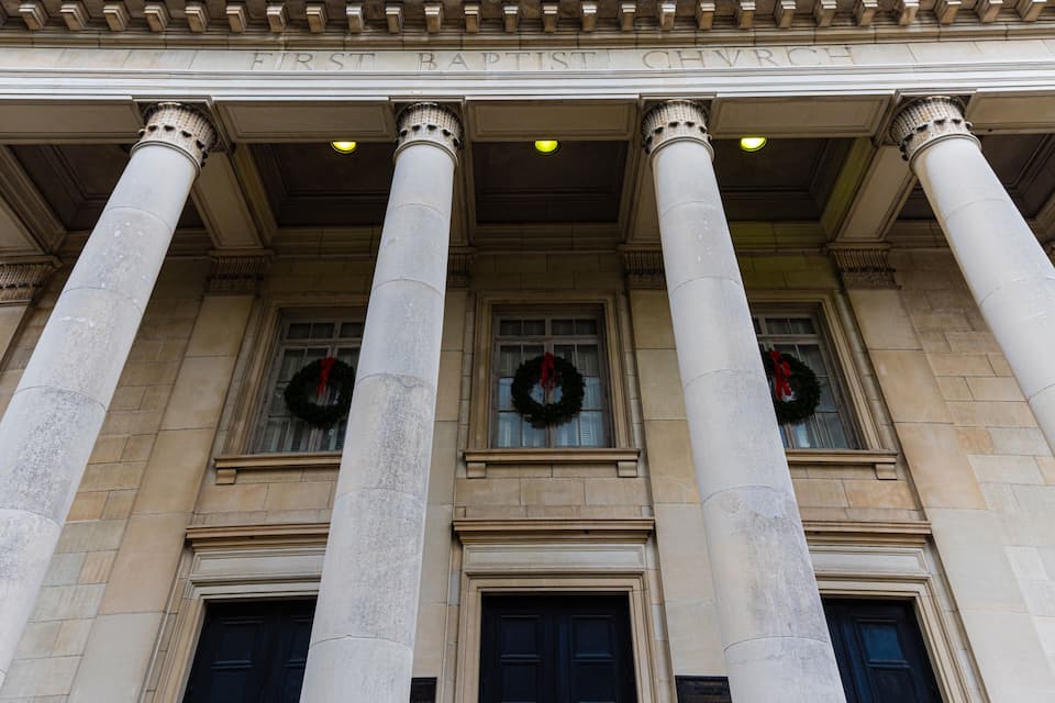 A neoclassical building facade with Corinthian columns, large doors, and wreaths on the windows.